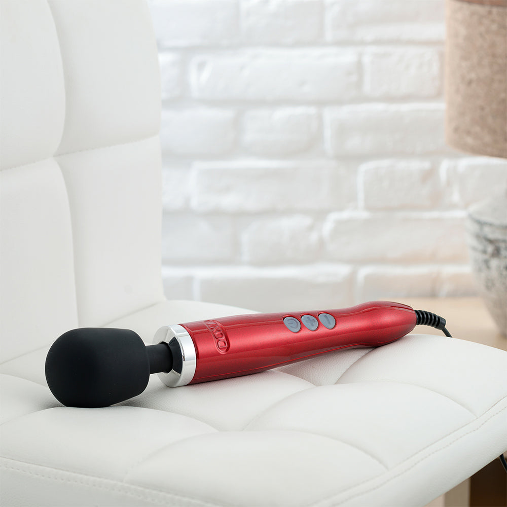 Doxy Die Cast Candy Red wand vibrator lying on a couch, ideal for hands-free use and relaxation. Shop this premium vibrator at SugarX in the Vibrators Collection.