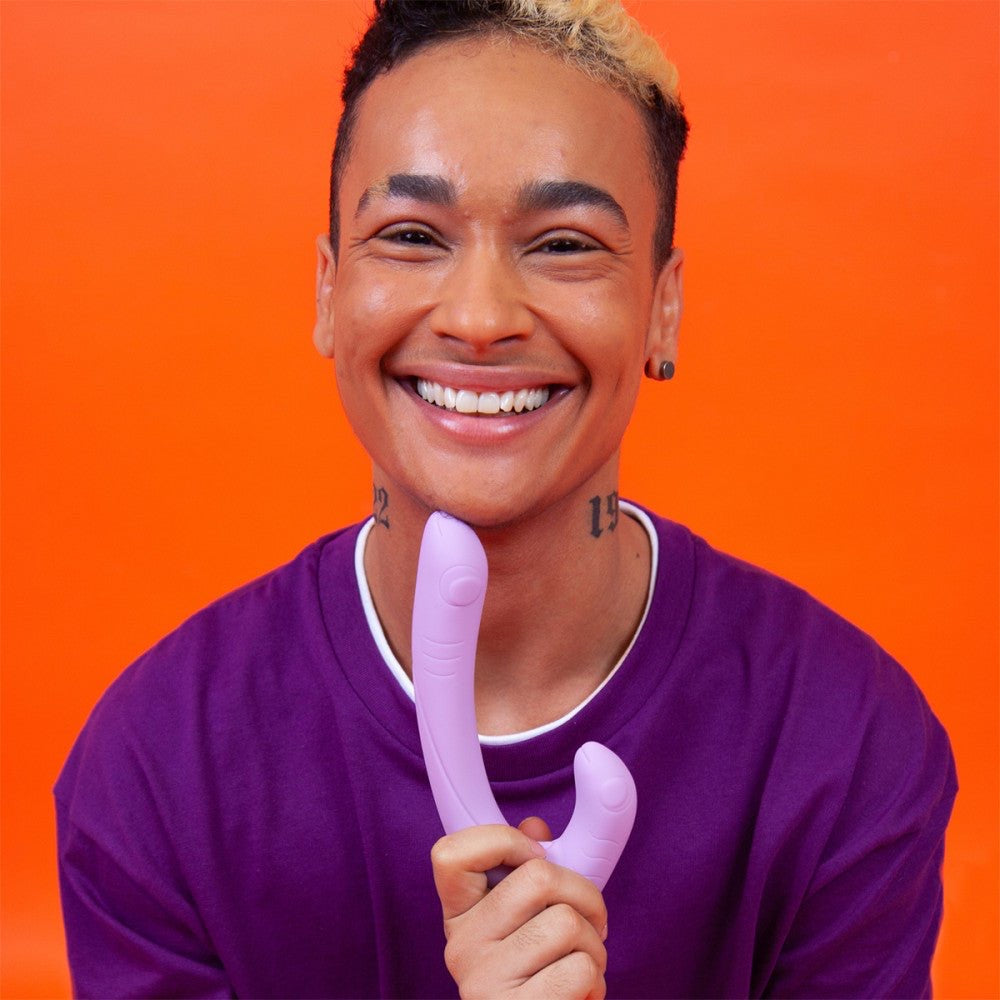 Smiling person holding Jix vibrator by Cute Little Fuckers in front of an orange background.