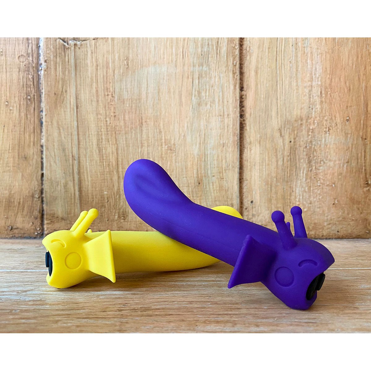 Shimmer vibrators in Midnight and Sunshine colors side-by-side in front of wood paneling. Ergonomic and beginner-friendly, from SugarX.