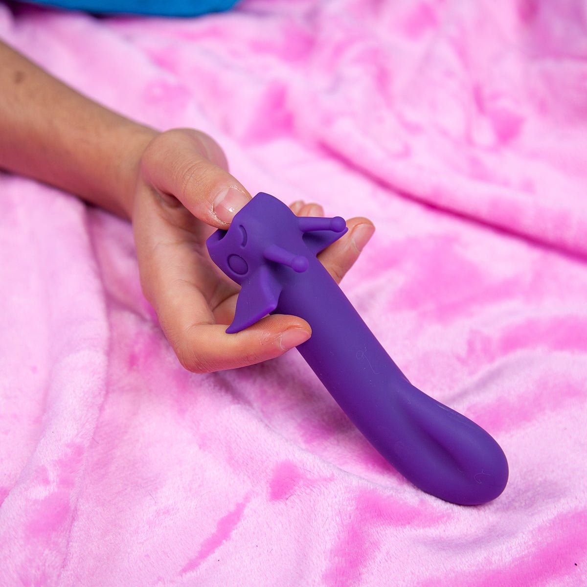 Shimmer Midnight vibrator held in front of a cozy pink blanket. Compact and versatile sex toy for all bodies, sold by SugarX.
