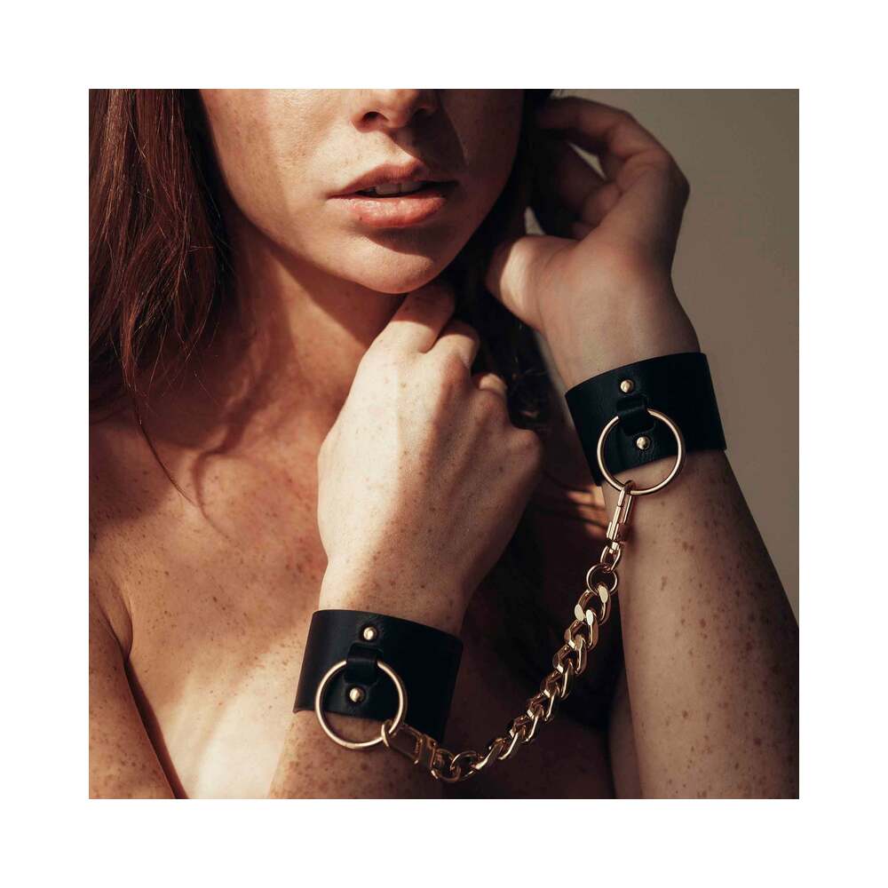 Bijoux Indiscrets Maze Wide Cuffs on a model showcasing the vegan leather material and gold chain. Available at SugarX in the BDSM Fashion collection of the Sex-Positive accessories section.