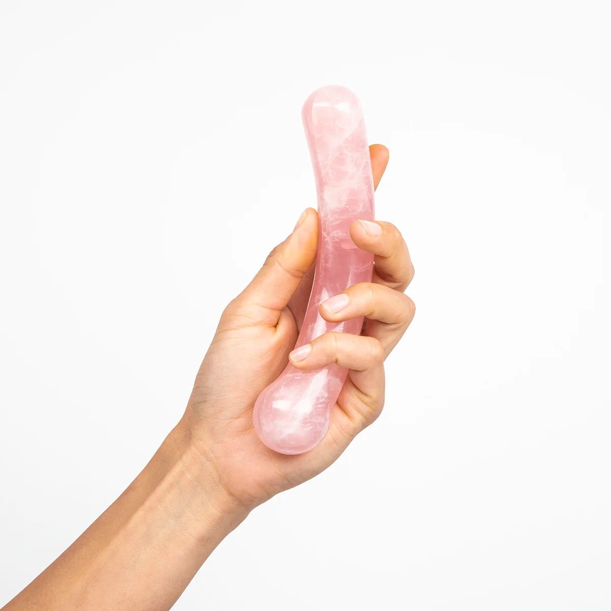 The Heart Curve by Chakrubs, a non-phallic rose quartz crystal dildo being held by a hand a white background. Available at SugarX in Sex Toys in the Dildo collection.