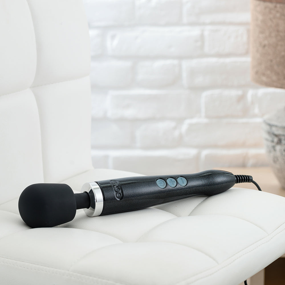 Doxy Die Cast Black wand vibrator lying on a couch, blending luxury and relaxation with its powerful performance. Available at SugarX in the Vibrators Collection.