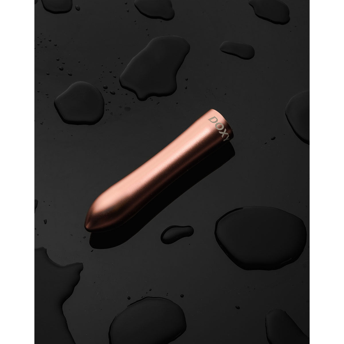 Doxy Bullet vibrator lying diagonally on a black background, accentuating its luxurious rose gold finish and compact design for portability. Available at SugarX in the Vibrators Collection.