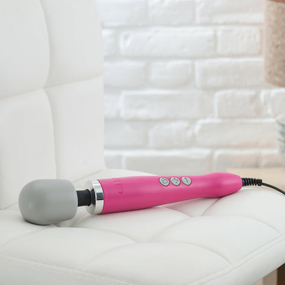 Doxy Original Massager vibrating wand in pink laying on a couch. Available at SugarX in the Vibrators Collection.